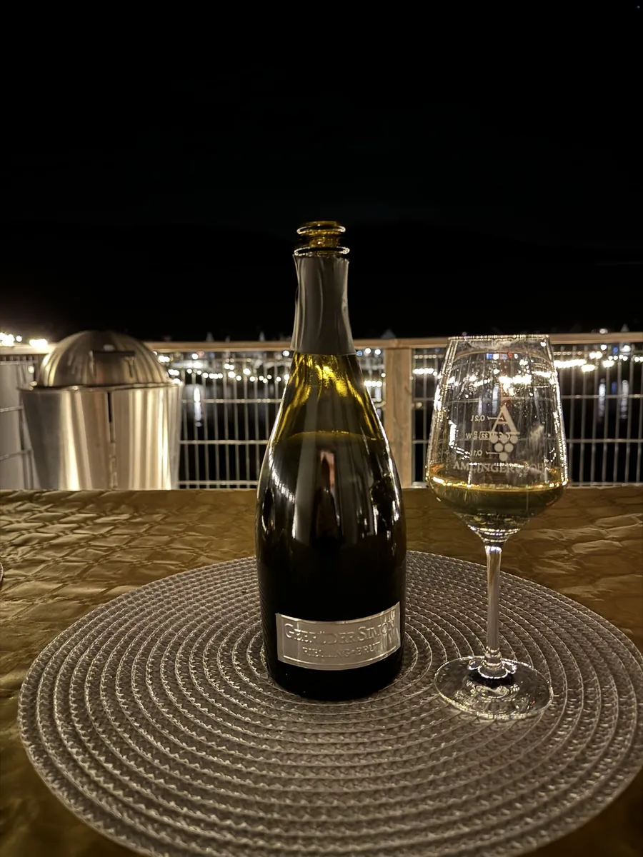 Flasche Gebrüder Simon Riesling Brut und ein Glas abends auf dem Balkon